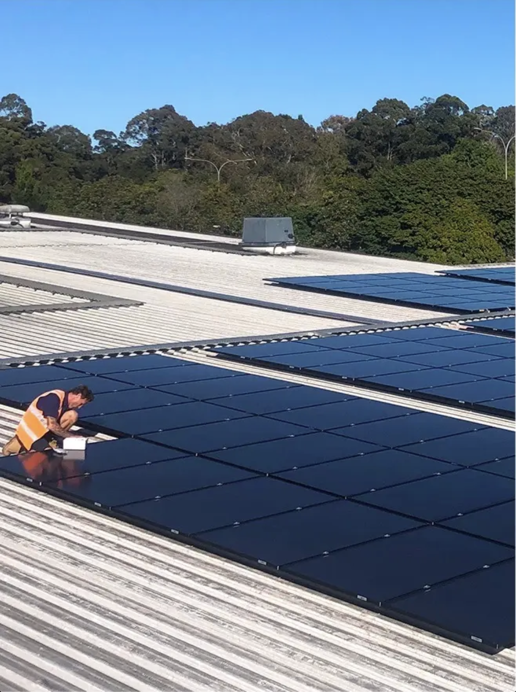 A worker installing solar panels across a large rooftop.